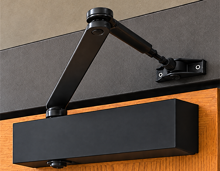 Black surface-mounted door closer fitted to a timber commercial entrance door